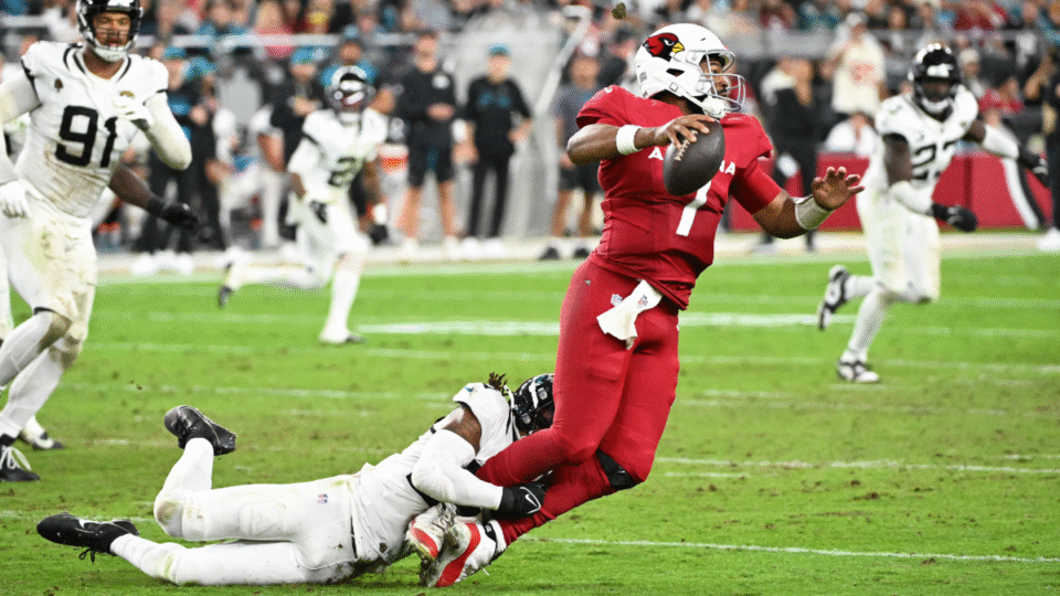 Jacoby Brissett #7 of the Arizona Cardinals is sacked by Cam'Ron Silmon-Craig #24 of the Jacksonville Jaguars in the fourth quarter of a game at State Farm Stadium on November 23, 2025 in Glendale, Arizona.