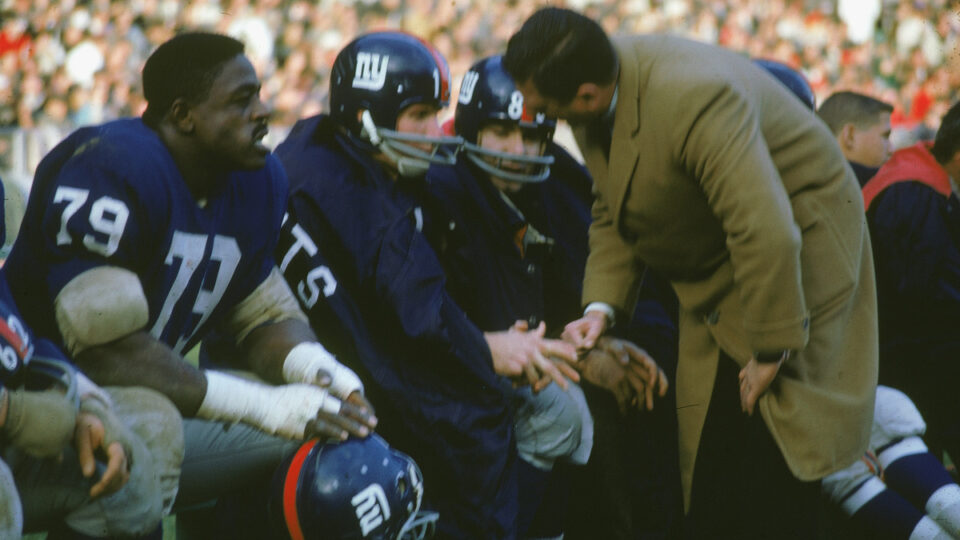 American professional football players Roosevelt 'Rosey' Brown (1932 - 2004), #79, and Y.A. Tittle of the New York Giants sit on the bench as head coach Allie Sherman bends over to talk with Tittle, November 1961.